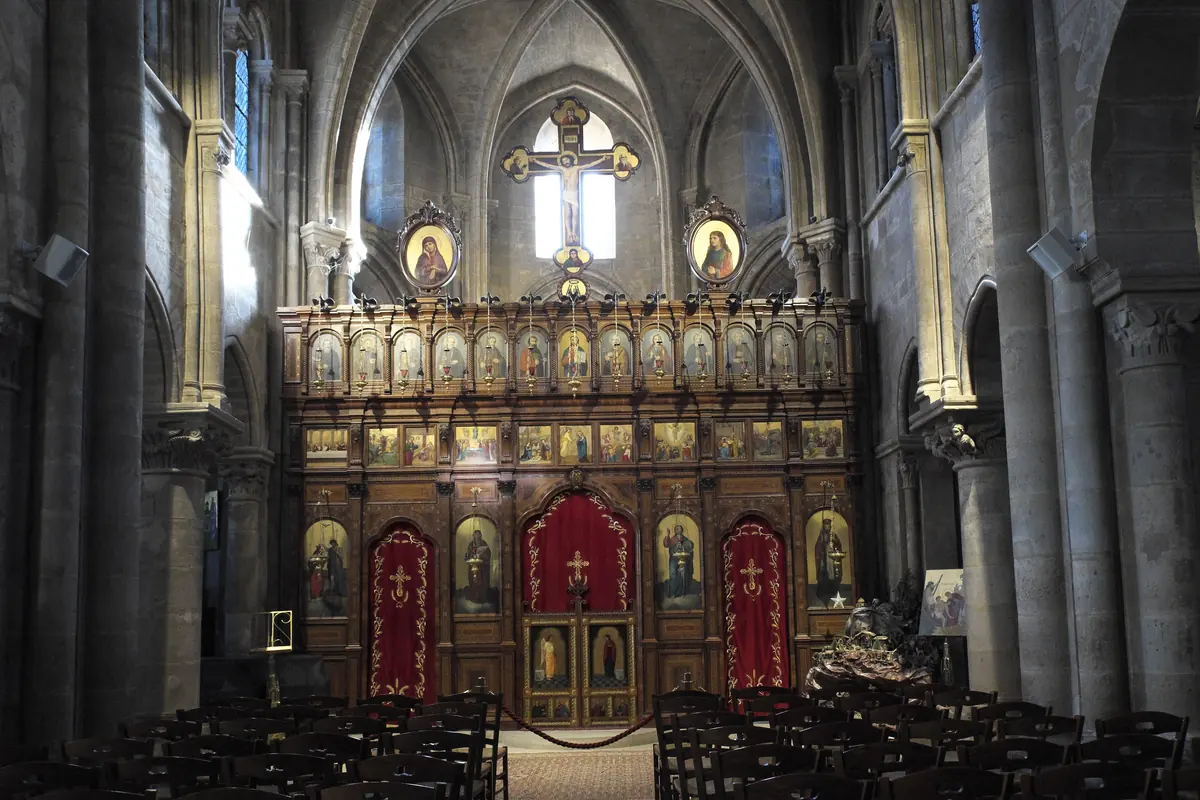 The carved wooden iconostasis of Saint-Julien-le-Pauvre with rows of painted icons and red curtains between the medieval columns of the nave.